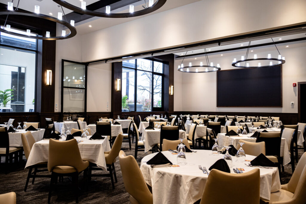 Private dining room at Chama Gaúcha San Antonio featuring round tables with white linens, leather chairs, modern lighting, and a sophisticated event space.