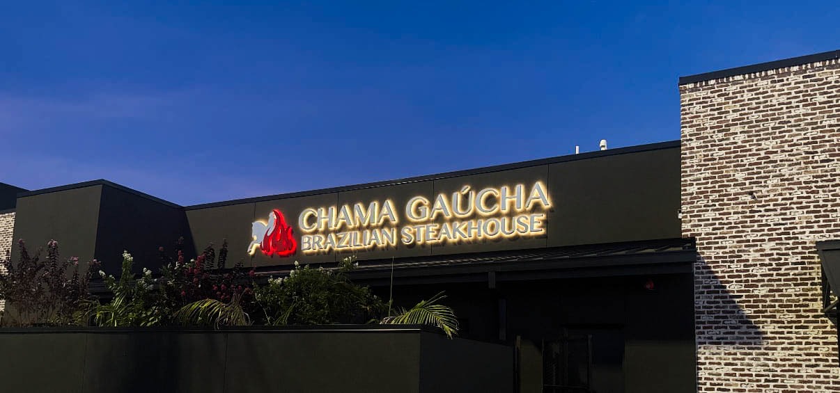 Exterior of Chama Gaucha Brazilian Steakhouse in Katy, Texas, illuminated signage and stone facade